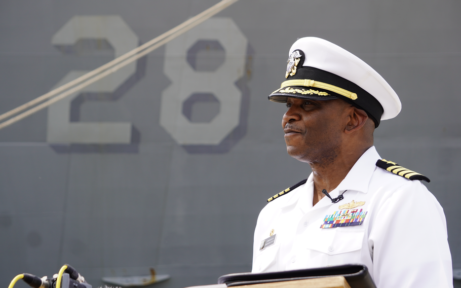 Capt. Jiwan A. Mack smiles with the USS Fort Lauderdale in the background.